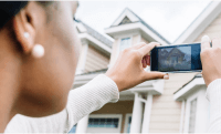 A woman using a mobile device to take a picture of a residential home